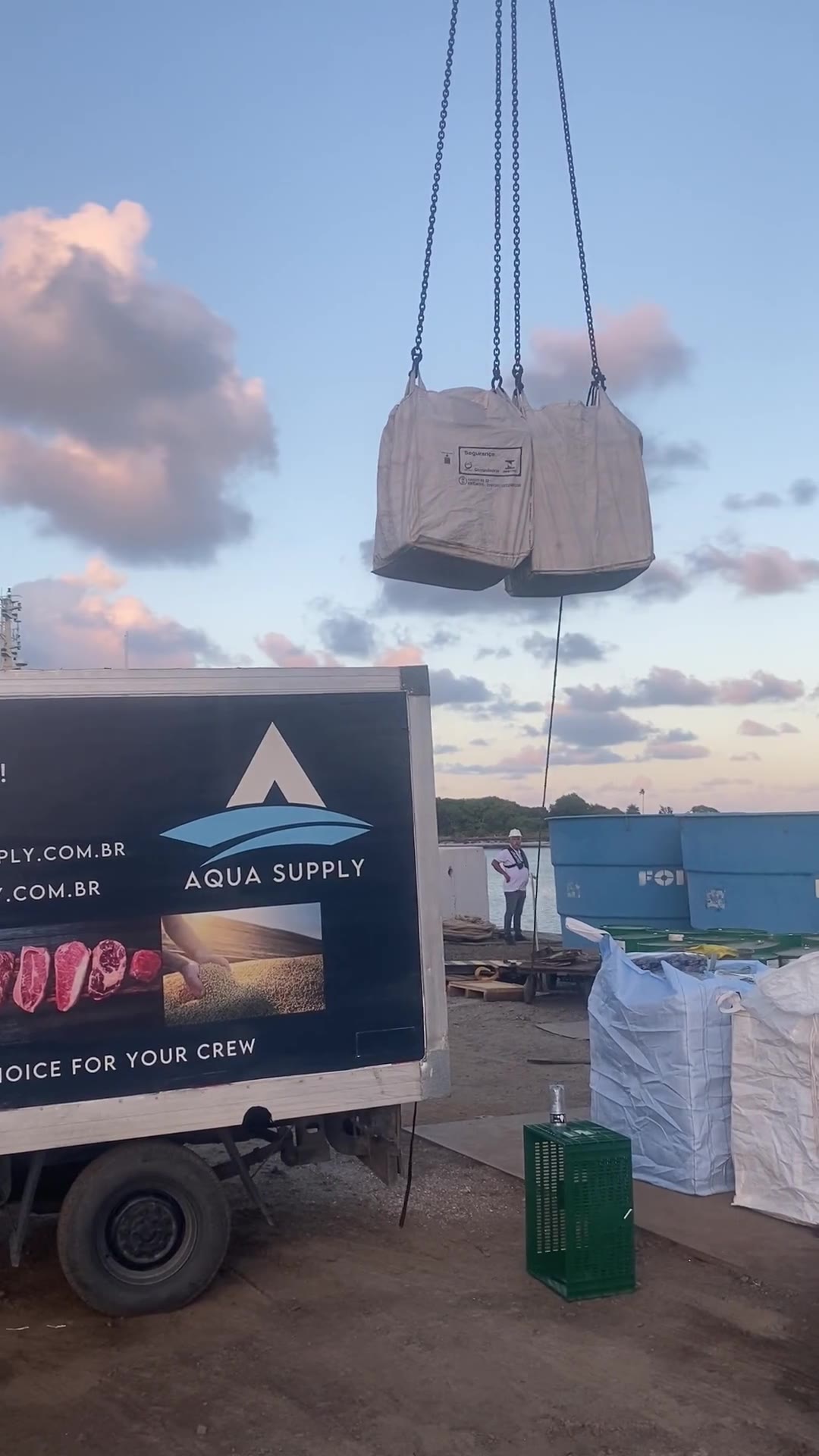 Caminhão da Aqua Supply no cais durante entrega a uma embarcação, com guindaste movimentando carga